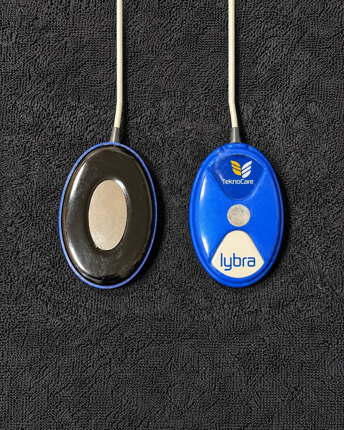 Zwei Lybra-Elektroden auf einem Handtuch: links die Kontaktfläche, rechts die Vorderseite mit Logo