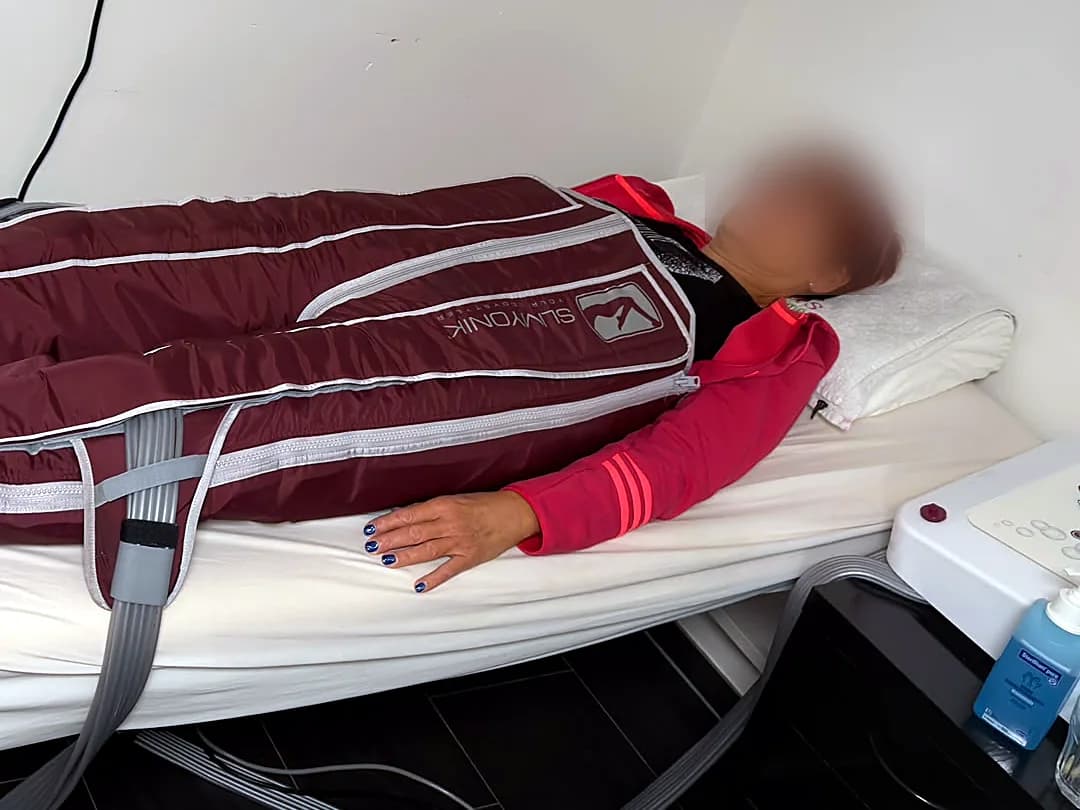 Kundin liegt in den Druckmanschetten auf der Behandlungsliege, daneben das Gerät